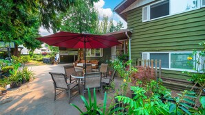 A patio with a table and chairs, surrounded by potted plants and a red umbrella. - Cozy 2BR Villa · Garden View · Near Beach, local specialties Provided as gift 
 (Surrey)