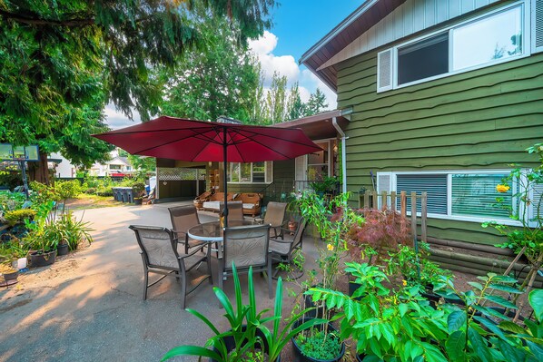 A patio with a table and chairs, surrounded by potted plants and a red umbrella.
