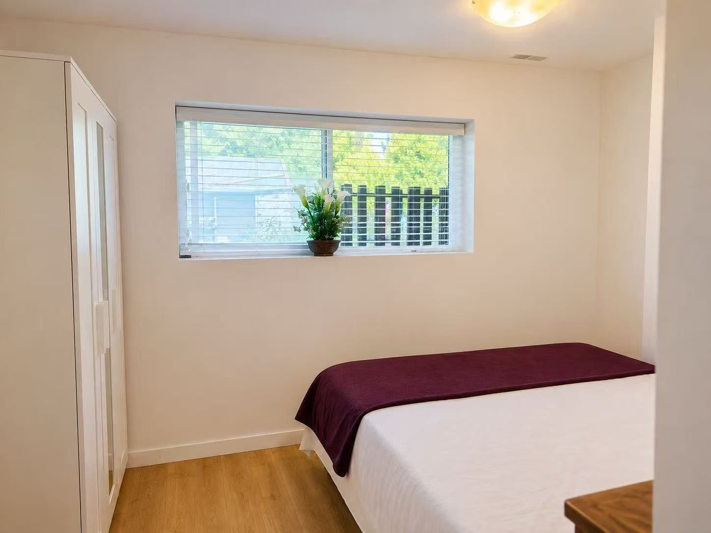 Ein Schlafzimmer mit einem Bett, einem Fenster mit Blick auf einen Zaun und einem Blumentopf auf dem Fensterbrett.