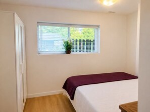 A bedroom with a bed, a window with a view of a fence, and a potted plant on the windowsill.