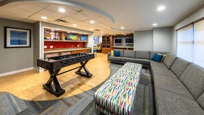 Ein modernes Wohnzimmer mit einem Kicker, einer Couch, einer farbenfrohen Bank und einer Bar mit einem Fernseher.