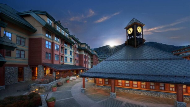 Ein Hotel mit einem Glockenturm, mehreren Gebäuden mit Balkonen und einer Bergkulisse.