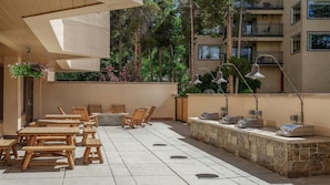 Eine Terrasse im Freien mit Holztischen und -stühlen, einer Steinsäule und einem hängenden Blumenkorb.