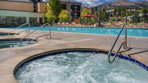 Un espace avec un jacuzzi, une piscine, des chaises longues et une vue sur les montagnes.