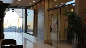 Un moderno vestíbulo de hotel con entrada de vidrio, una zona de estar con sillas y una planta grande en maceta.
