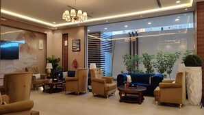Un moderno hall de hotel con un amplio espacio de descanso, un televisor de pantalla plana y un ventanal con vistas a la ciudad.