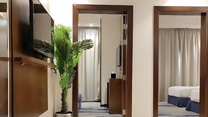 Un pasillo de hotel con una planta grande en maceta, un televisor de pantalla plana montado en la pared y una cama visible a través de una puerta abierta.