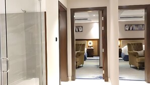 Un pasillo moderno de hotel con ducha de vidrio, puerta de madera y una cama al fondo.