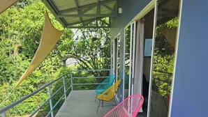Un balcon doté d’une rambarde en métal, d’un sol en béton et de trois chaises colorées.