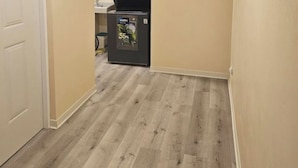 Un couloir avec un parquet en bois clair, une porte blanche et un réfrigérateur au fond.