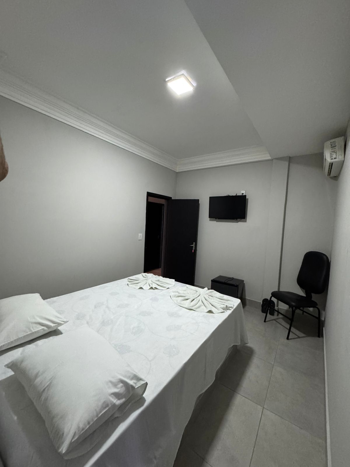 Hotellihuone, jossa on sänky, tuoli, televisio ja ilmastointilaite.