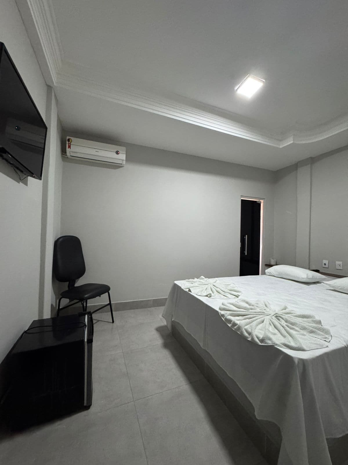 Habitación de hotel con cama, una silla, un escritorio, un equipo de aire acondicionado y un televisor en la pared.