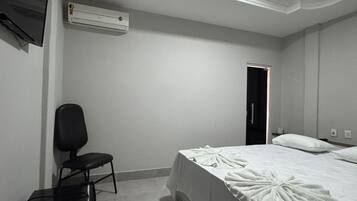 Habitación de hotel con cama, una silla, un escritorio, un equipo de aire acondicionado y un televisor en la pared.