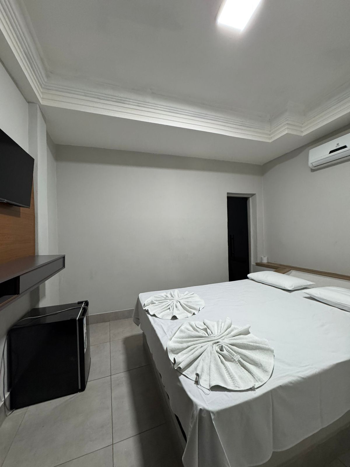 Een hotelkamer met een bed, een aan de muur bevestigde televisie, een prullenbak en een airconditioning.
