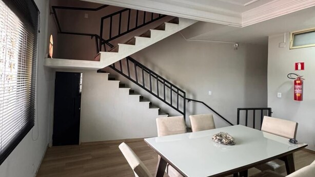 A modern interior with a dining area featuring a white table and four chairs, a staircase with black railings, and a fire extinguisher mounted on the wall.