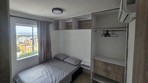 Une chambre à coucher avec un lit, une fenêtre donnant sur des immeubles, une armoire et un luminaire au plafond.