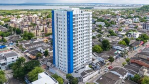 Un immeuble de grande hauteur à l’architecture moderne, situé dans un quartier urbain densément peuplé, entouré de divers bâtiments et d’espaces verts.