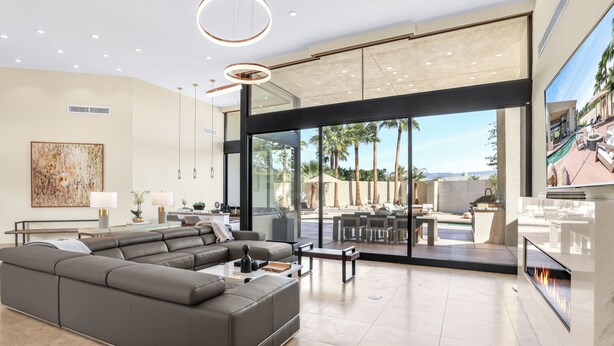 Un salon moderne avec un canapé d’angle, une cheminée et de grandes portes vitrées donnant sur une terrasse extérieure.