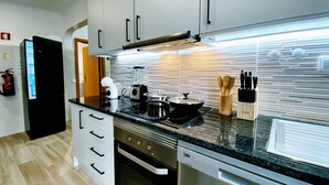 A modern kitchen with a black refrigerator, a stove, an oven, and a dishwasher. There is a blender on the counter and a knife block with wooden spoons.