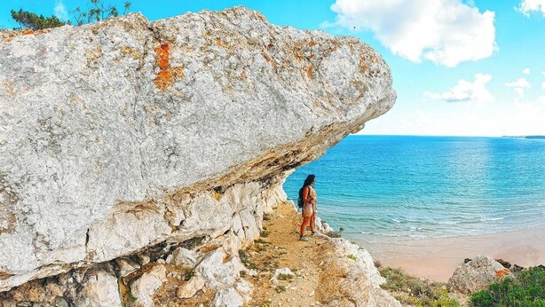 A coastal landscape with a large rock formation and a beach.