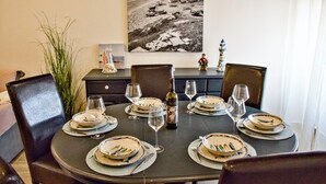 A dining table set with plates, glasses, and cutlery, surrounded by chairs, with a decorative item and a bottle on the table.