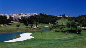 A golf course with sand bunkers, a pond, and a backdrop of residential buildings.