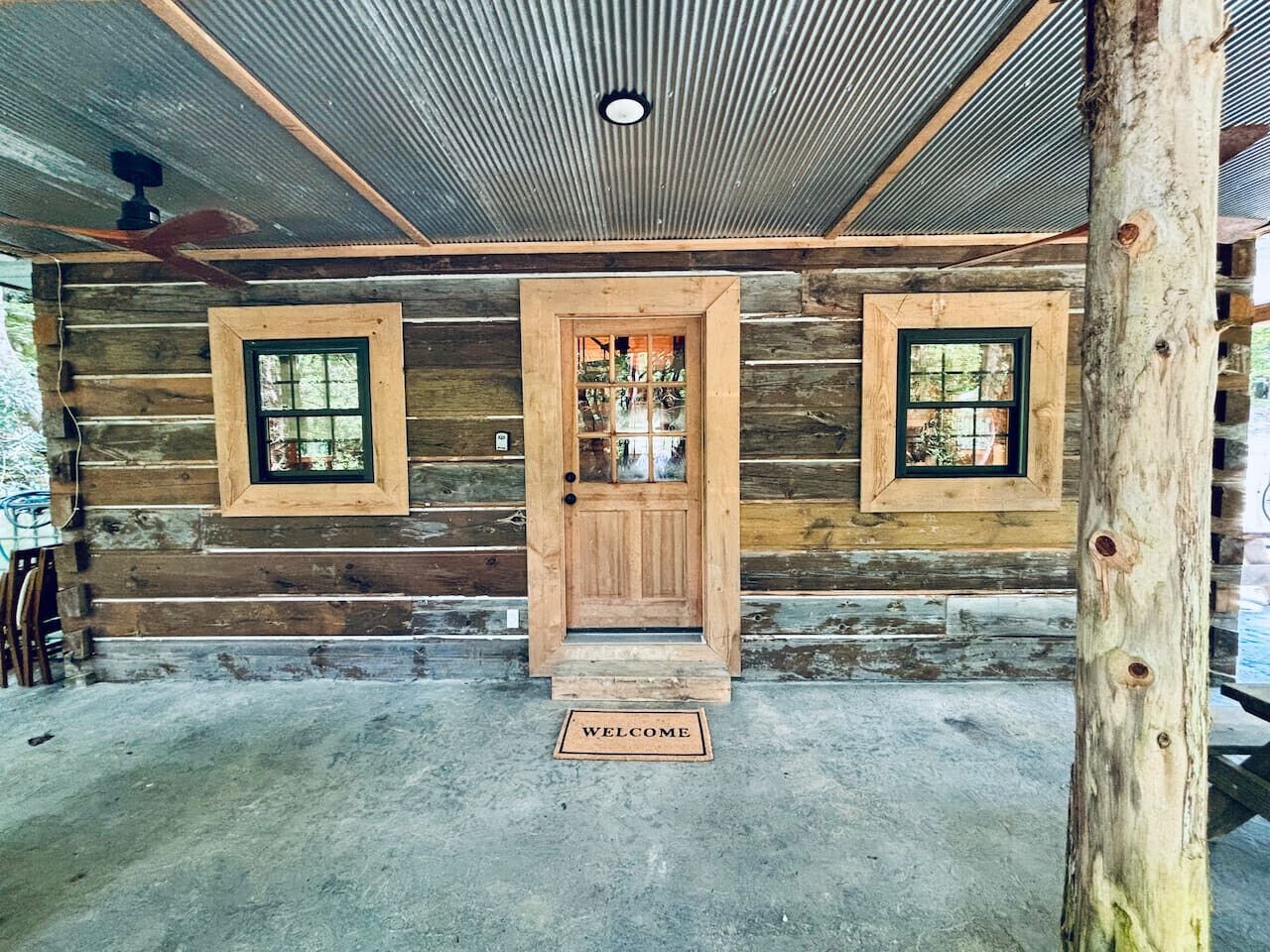 A log cabin with a wooden door, two windows, and a welcome mat.