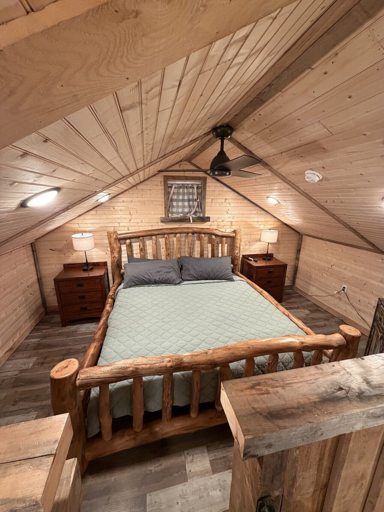 Un letto con struttura in legno in una stanza a soffitto spiovente, con una finestra e due comodini.