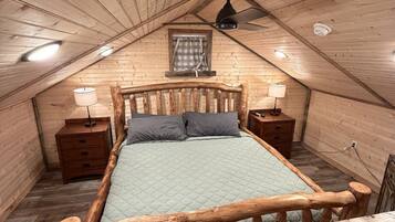 Un letto con struttura in legno in una stanza a soffitto spiovente, con una finestra e due comodini.