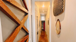 Un pasillo con suelo de madera, una puerta de madera con diseño geométrico, un espejo montado en la pared y un tapiz mural estampado.