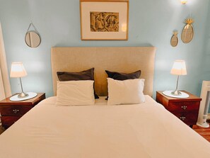 A neatly made bed with white linens, two bedside lamps, and a framed artwork above the headboard.