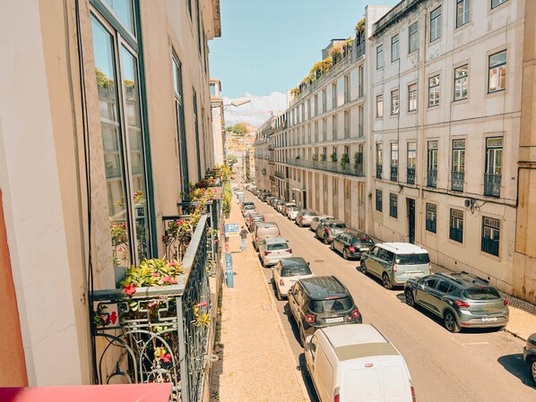 A narrow street lined with parked cars and buildings with balconies.