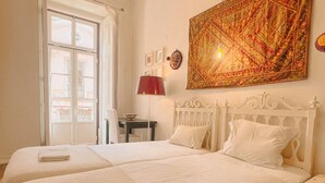 Habitación de hotel con dos camas, una mesa de comedor, una lámpara roja y un tapiz grande en la pared.