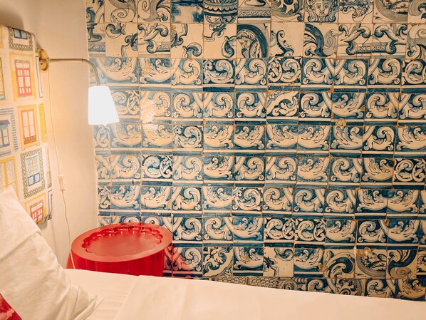 Un baño con pared de azulejos con diseños intrincados en azul y blanco, un lavabo rojo y una toalla blanca colgada en un perchero.