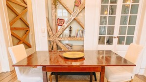 Una mesa de comedor con un camino de mesa tejido, dos sillas blancas con acolchado y piso de madera.