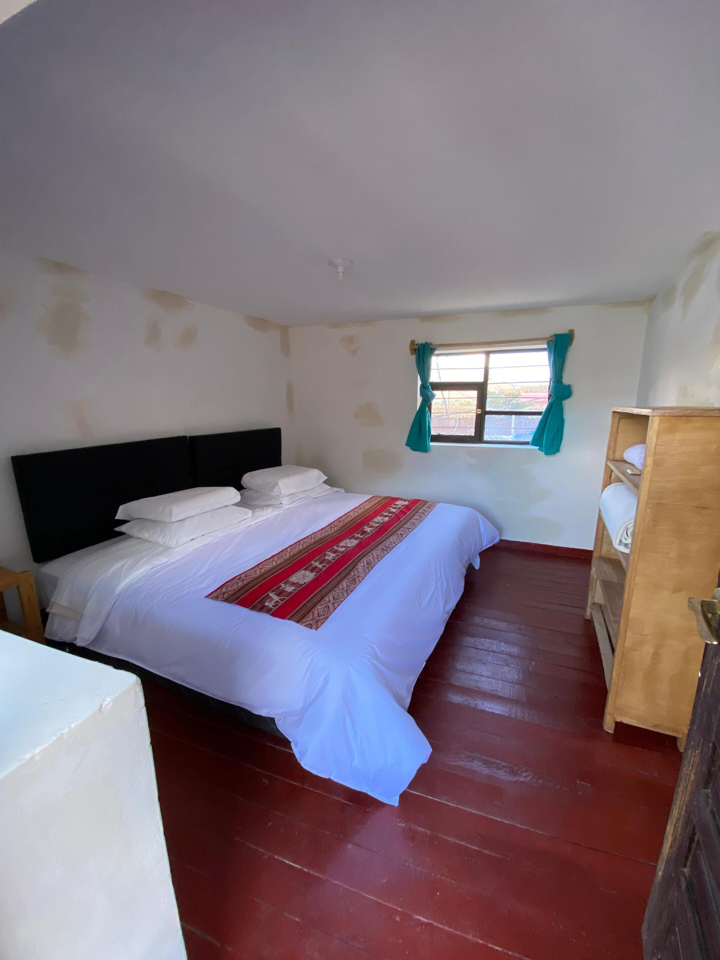 A bedroom with a bed, a wooden wardrobe, and a window with curtains.