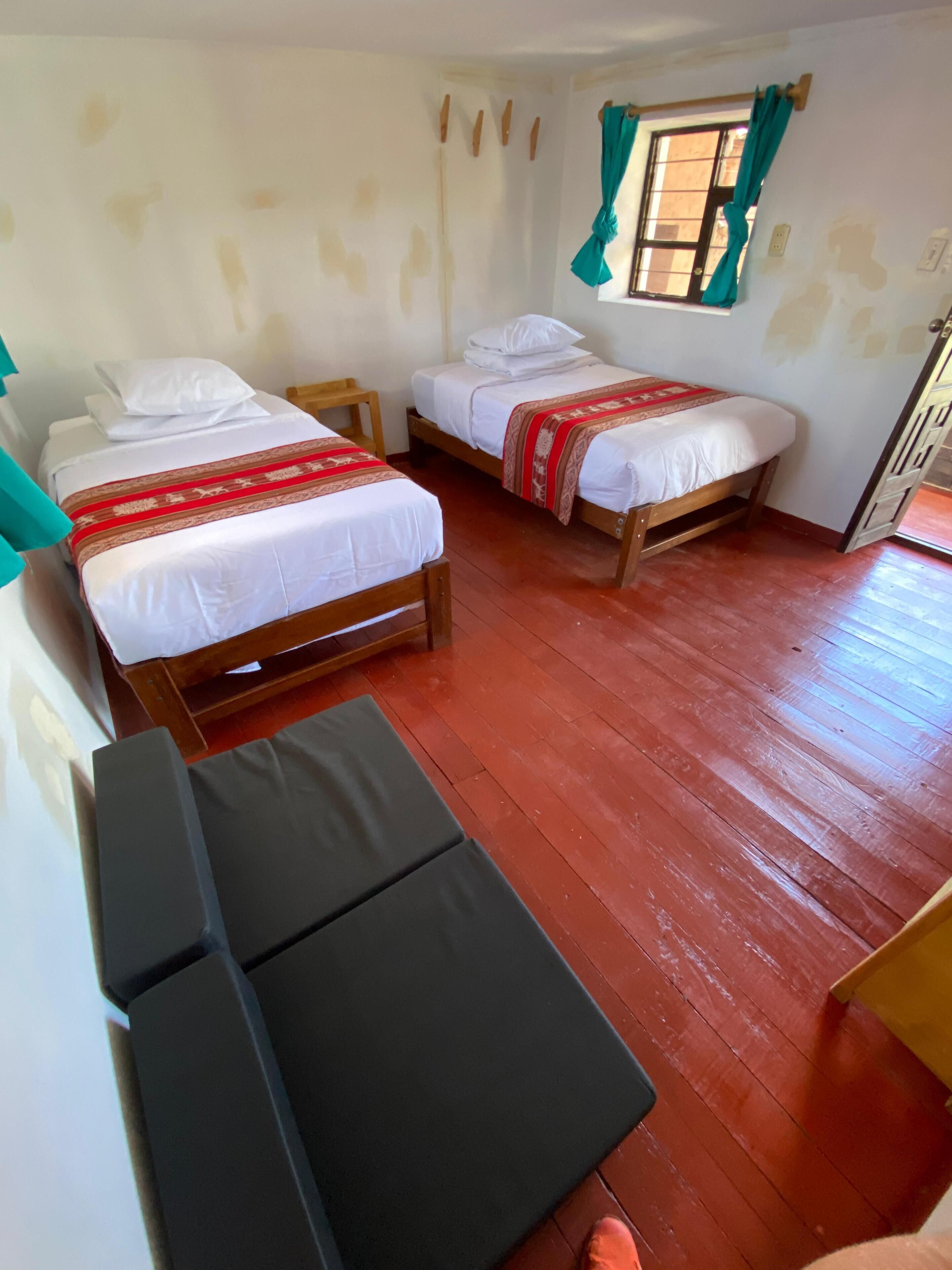 A room with two wooden beds, a small table, and a window with curtains.