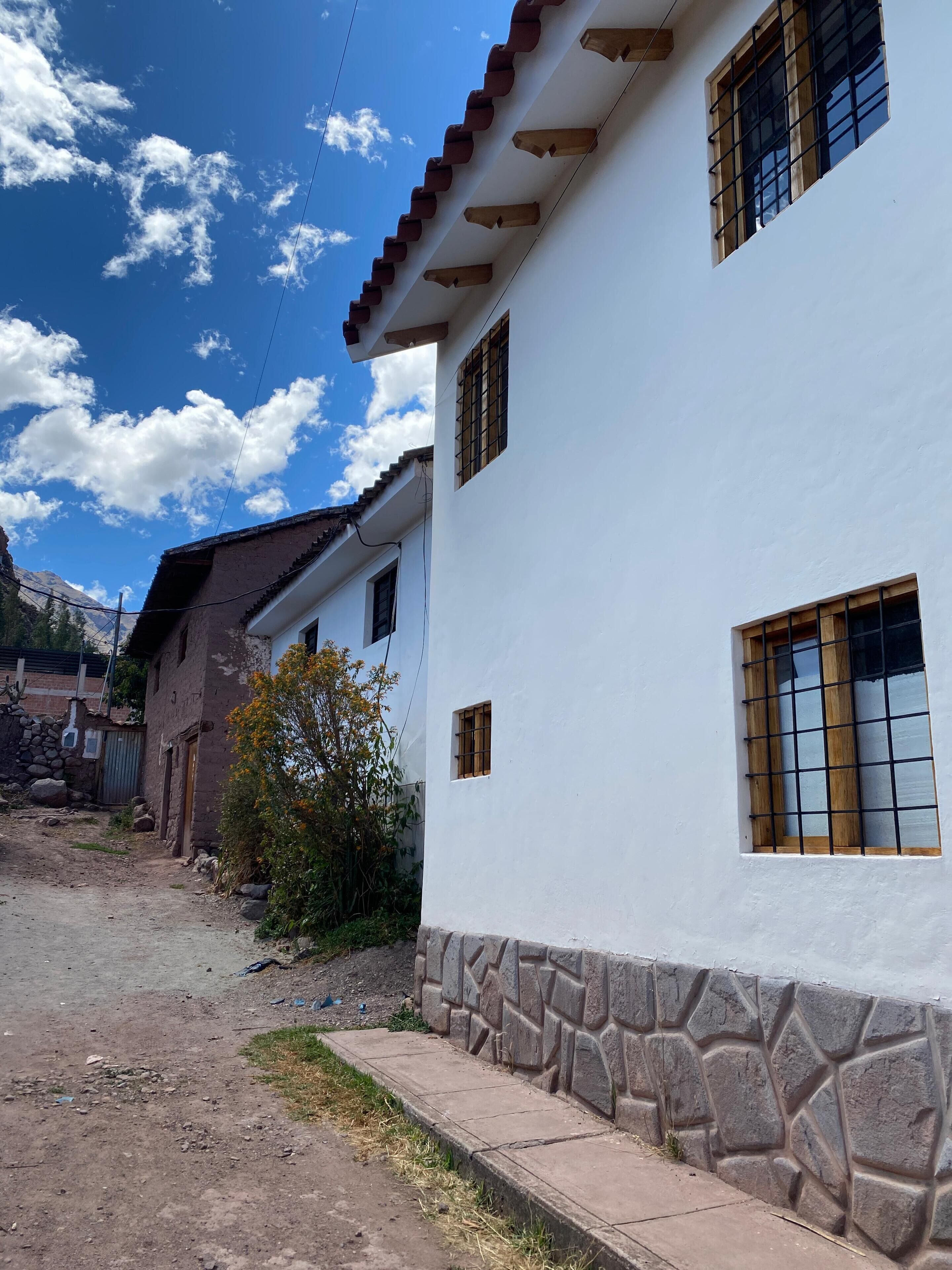 A white building with stone accents, a dirt path, and a clear blue sky with clouds.