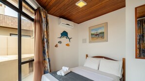 A hotel room with a bed, a window with curtains, an air conditioning unit, a painting on the wall, and a view of the outside balcony.