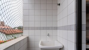 Un baño pequeño y cerrado con un lavamanos blanco, paredes con azulejos y vistas a través de una cerca de alambre.