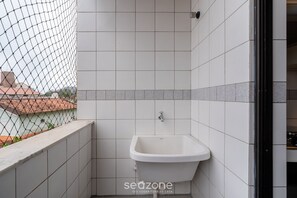 Een kleine, afgesloten badkamer met een witte wastafel, betegelde muren en uitzicht door een hekwerk.