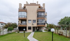 A modern multi-story residential building with balconies, large windows, and a well-maintained lawn.