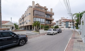 A multi-story residential building with balconies, a gated parking area, and a street view. - Apt w/ Pool & BBQ 150m from the sea - CND0204 (Florianópolis)