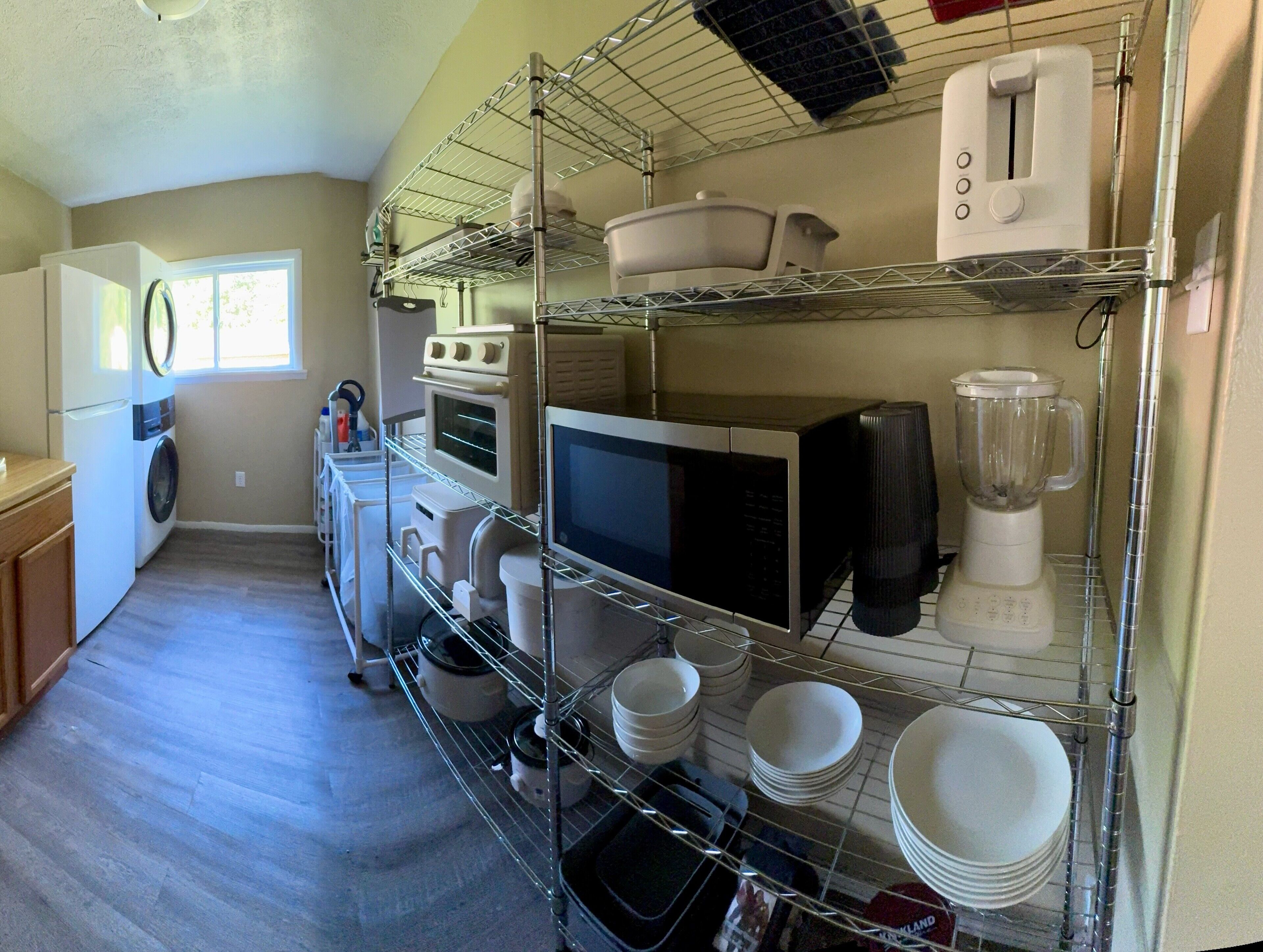 A compact kitchen with a washing machine, microwave, and a blender on shelves.