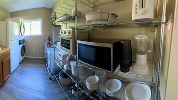 A compact kitchen with a washing machine, microwave, and a blender on shelves.