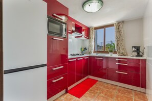 Eine Küche mit roten Schränken, einer Mikrowelle, einem Herd und einem Fenster mit Vorhängen.
