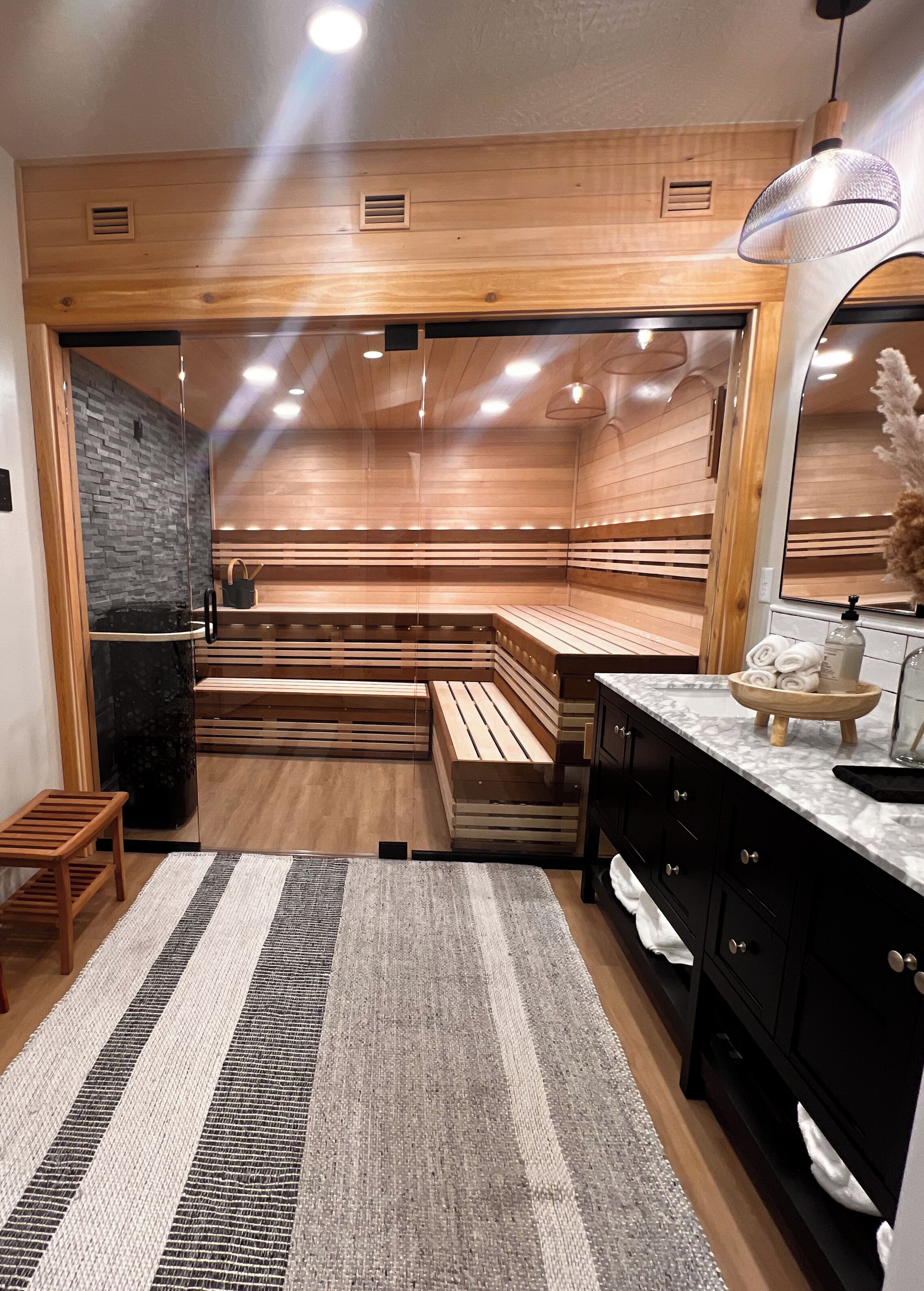 Uma sauna moderna com bancos de madeira, porta de vidro e bancada de mármore com toalhas.