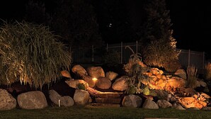 Een hottub met een stenen omlijsting en een klein watervalletje, omgeven door rotsen en planten.