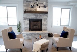 A living room with a stone fireplace, two armchairs, a coffee table, and a hanging light fixture.