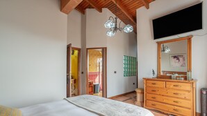 A bedroom with a bed, wooden dresser, TV, and a chandelier.
